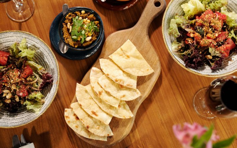 A colorful Mediterranean spread featuring pita, salads, and wine on a wooden table.